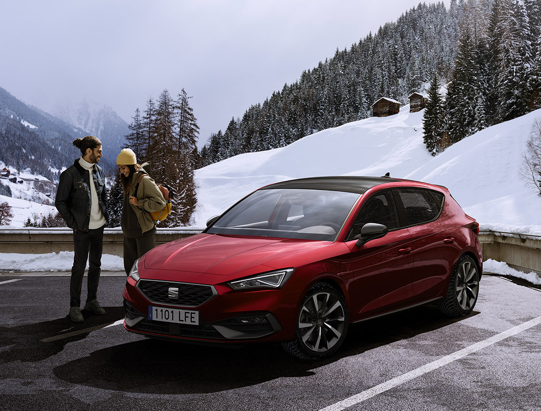 couple parlant à côté d'une seat leon de couleur desire red sur une montagne enneigée