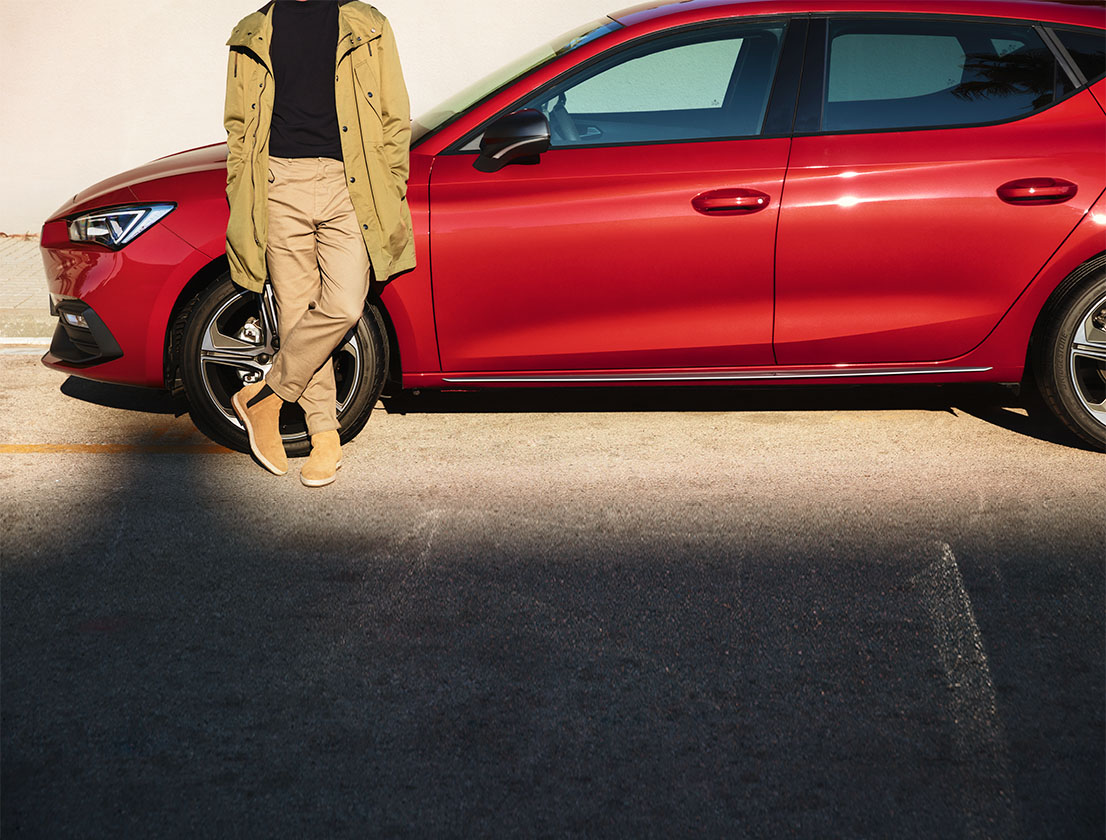 homme debout à côté d'une seat leon break de couleur desire red 